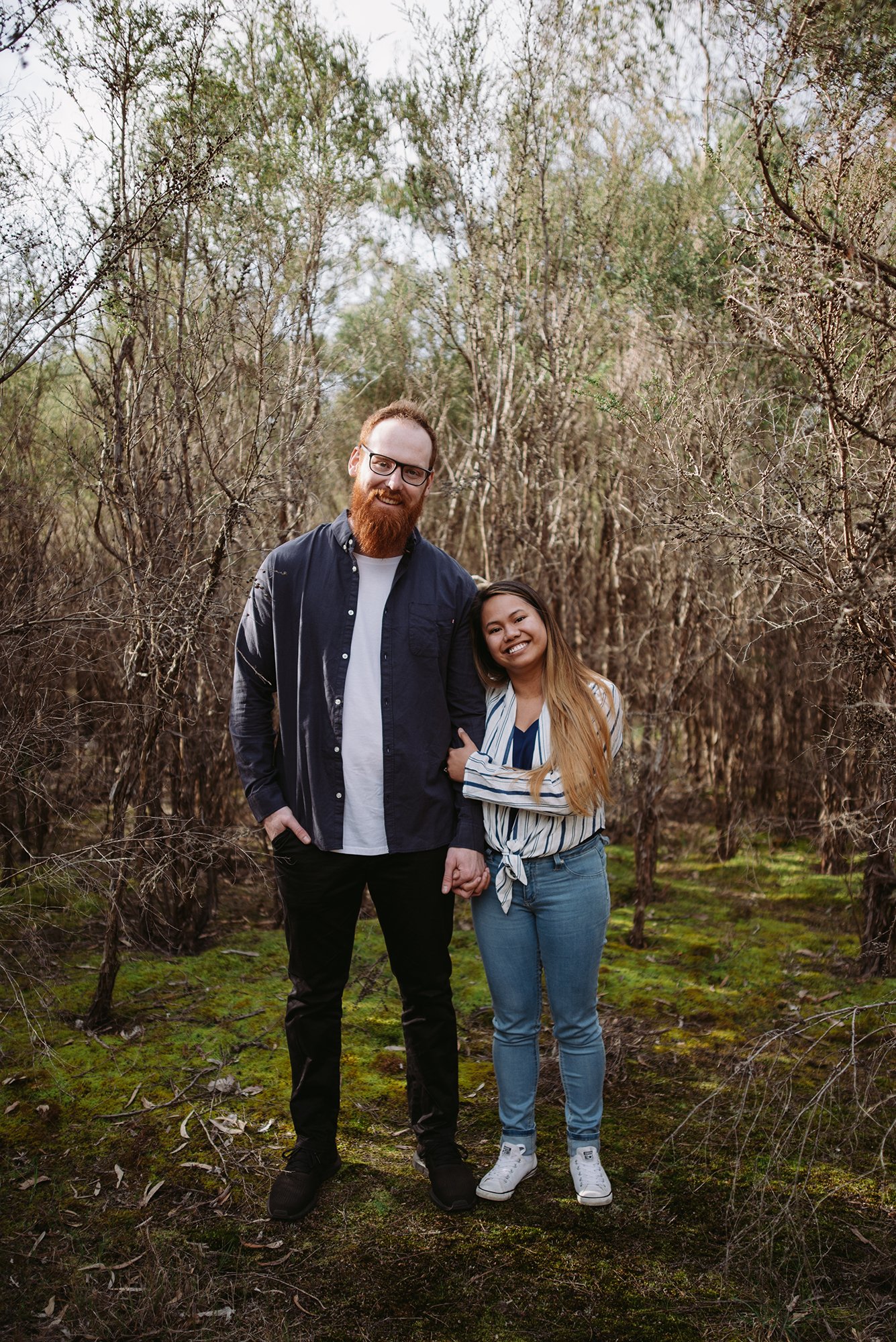 A couple are looking at the camera in a forest at this Mornington Peninsula Engagement Photo location