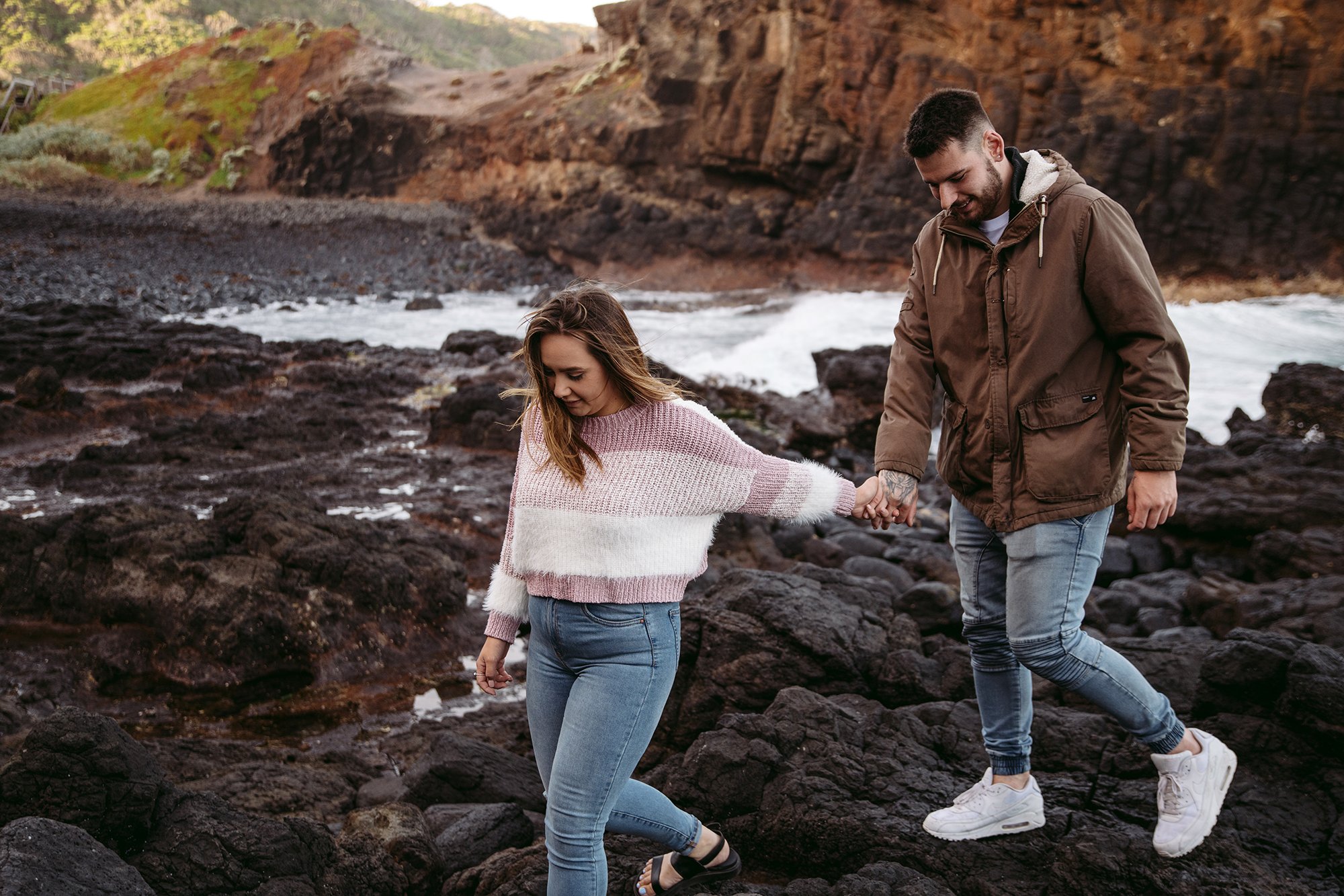 A couple are walking over rocks at the beach photo location on the Mornington Peninsula