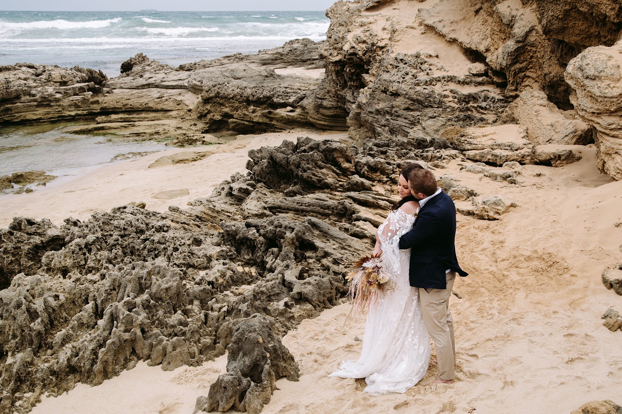 A wedding couple are cuddling up at the beach on their wedding day at this Mornington Peninsula Engagement Photo location