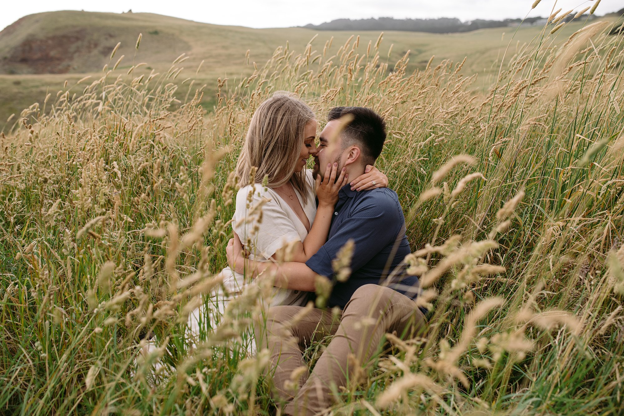 A couple are kissing in long grass at this Mornington Peninsula Engagement Photo location